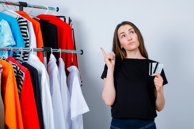 Free photo youg girl si thinking by looking up and holding credit cards on clothes background