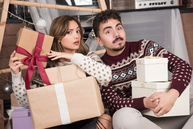 Young adorable couple sitting on the floor and posing with Christmas gifts.