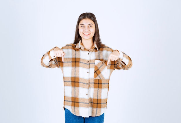 Free photo young adorable girl in casual outfit pointing at downside on white wall.