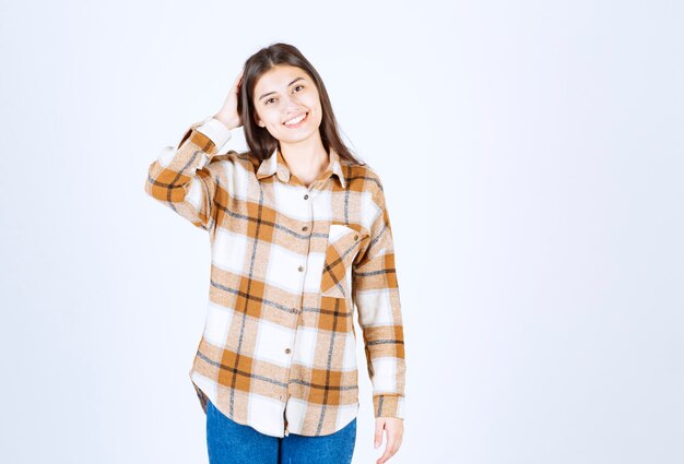 Young adorable girl in casual outfit posing to camera over white wall. 