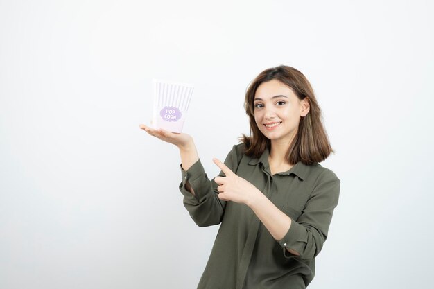 Young adorable woman pointing at popcorn box and posing. High quality photo