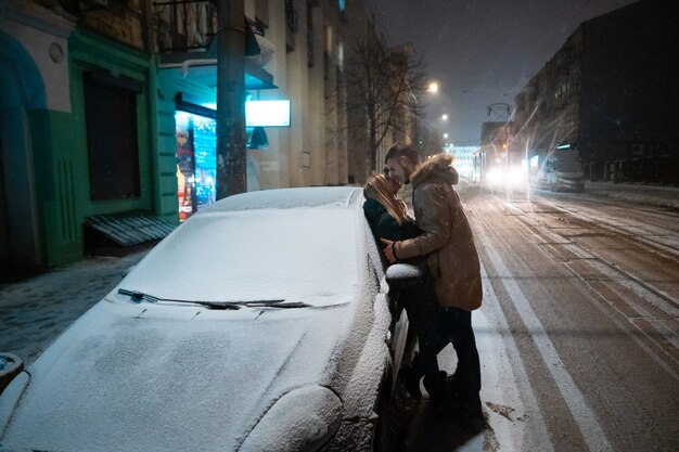 Young adult couple kissing each other on snow covered street