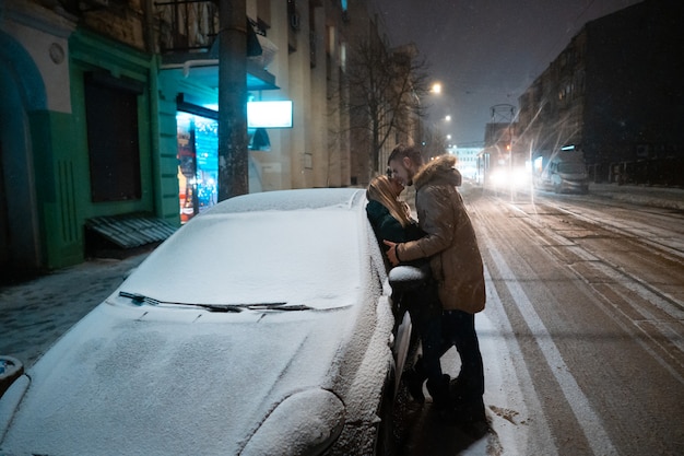 Young adult couple kissing each other on snow covered street