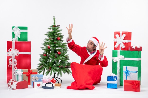 젊은 성인 선물 산타 클로스로 옷을 입고 8을 보여주는 바닥에 앉아 장식 된 크리스마스 트리