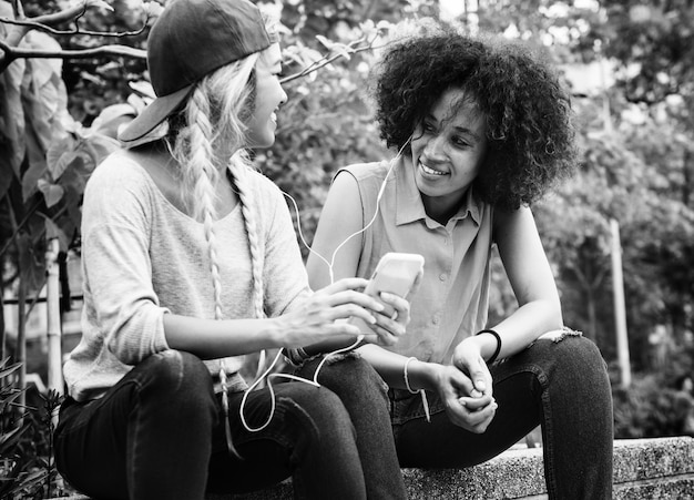 Foto gratuita giovani amici della femmina adulta che ascoltano la musica tramite il loro smartphone all'aperto