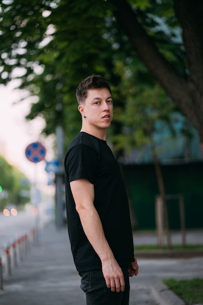 Young adult man in a black t-shirt and jeans walks on a city street