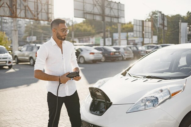 市内で電気自動車を充電している若い成人男性。エコ電気自動車のコンセプト。