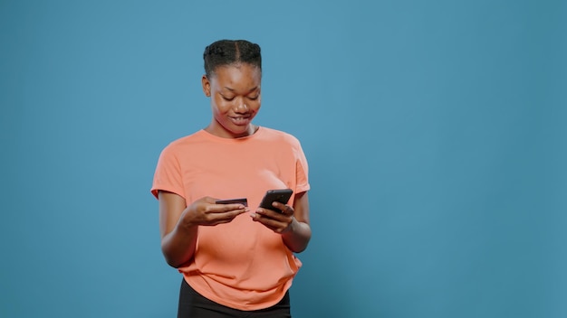 Young adult using credit card to make purchase on smartphone. Modern woman holding mobile phone to buy clothes on online shopping from retail store. Person doing payment transaction.