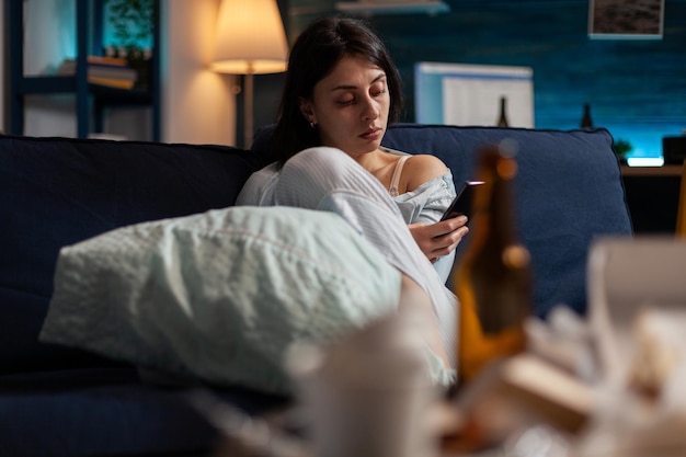 Free photo young adult with anxiety and suicidal thoughts using smartphone to browse internet and search website online. depressed woman with mental health illness using mobile technology on sofa.