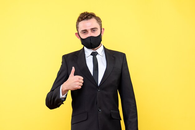 Young adult with suit and tie showing ok sign with his thumb up on yellow