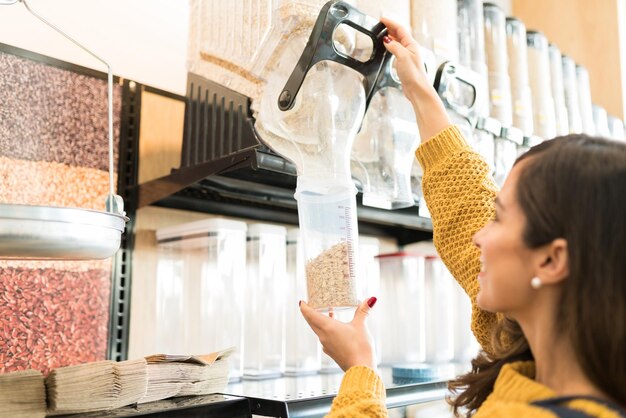 Young adult woman pouring cereal in container while buying in bulk at grocery store