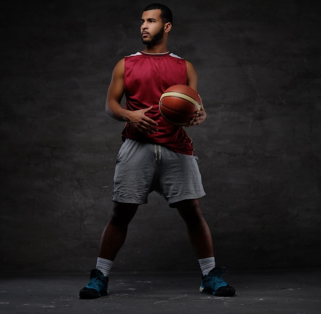 Free photo young african-american basketball player in sportswear playing with ball. isolated on a dark background.