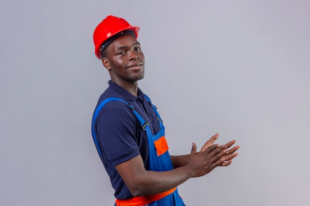 Young african american builder man wearing construction uniform and safety helmet applauding with smile on face standing 