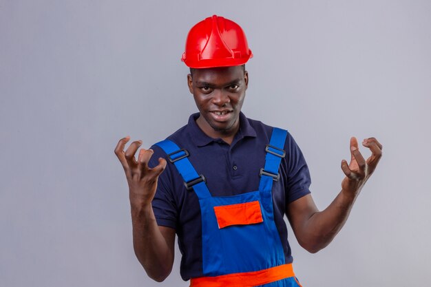 Young african american builder man wearing construction uniform and safety helmet crazy and mad standing with aggressive expression and arms raised standing 