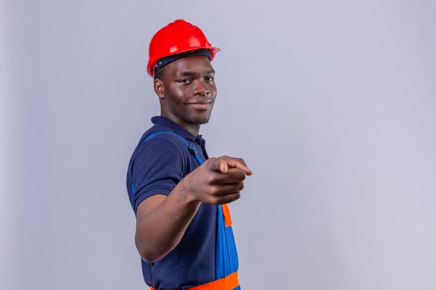 自信を持って笑顔で立っている建設の制服と安全ヘルメットの人差し指を着ている若いアフリカ系アメリカ人ビルダー男