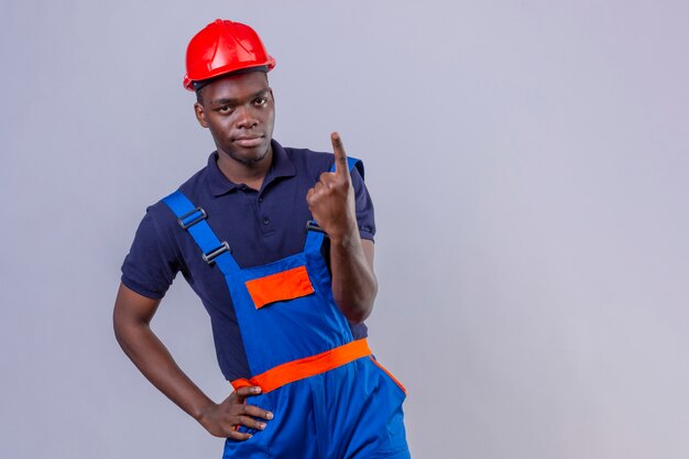 건설 유니폼과 안전 헬멧을 착용하는 젊은 아프리카 계 미국인 작성기 남자는 자신감이 서있는 찾고 번호 하나를 보여주는 검지 손가락으로 가리키는