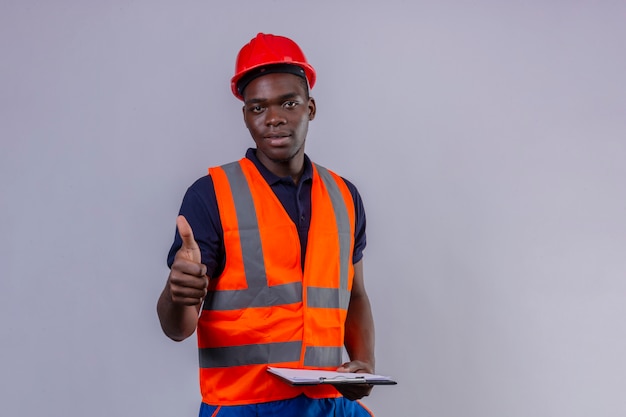 Young african american builder man wearing construction vest and safety helmet with smile on face showing thumb up standing 