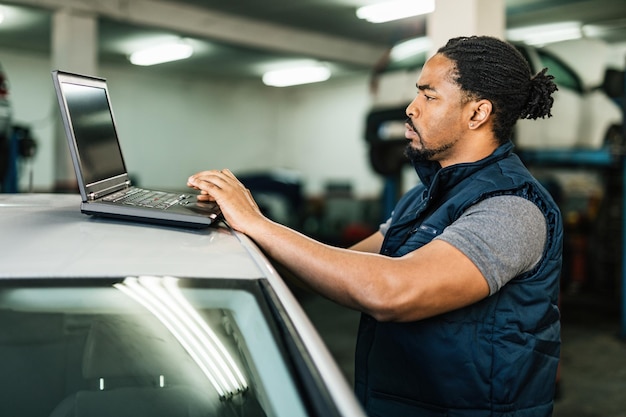 Foto gratuita giovane meccanico di auto afroamericano che utilizza il computer portatile in officina di riparazione