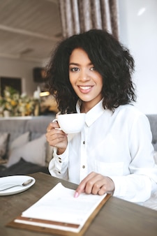 一​杯​の​コーヒー​と​レストラン​に​座っている​若い​アフリカ系​アメリカ人​の​女の子