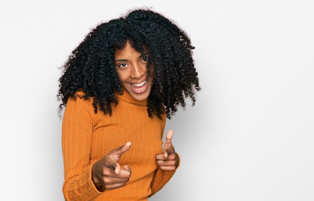 幸せで面白い顔でカメラに指を向けるカジュアルな服を着ている若いアフリカ系アメリカ人の女の子。良いエネルギーとバイブ。