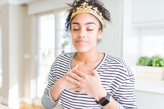 Young african american girl wearing golden queen crown on head smiling with hands on chest with closed eyes and grateful gesture on face Health concept