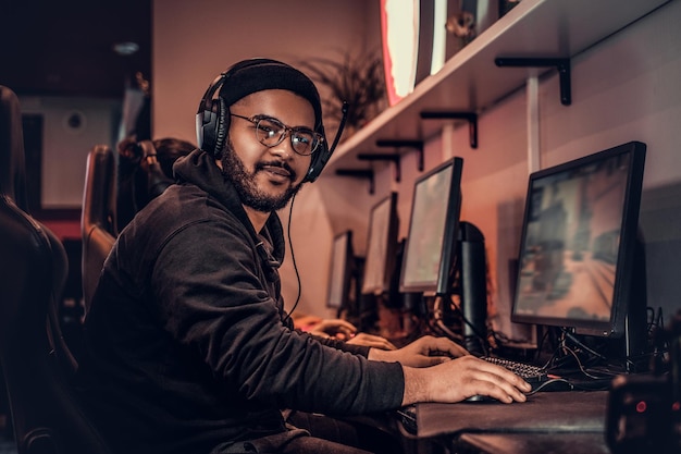 A young African American guy, enjoying spending time with his friends, playing in a multiplayer video game on a PC in a gaming club or internet cafe.