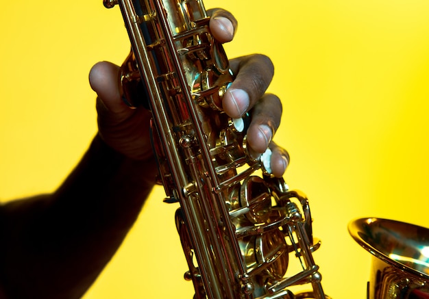 Young african-american jazz musician playing the saxophone on yellow  background in trendy neon light.