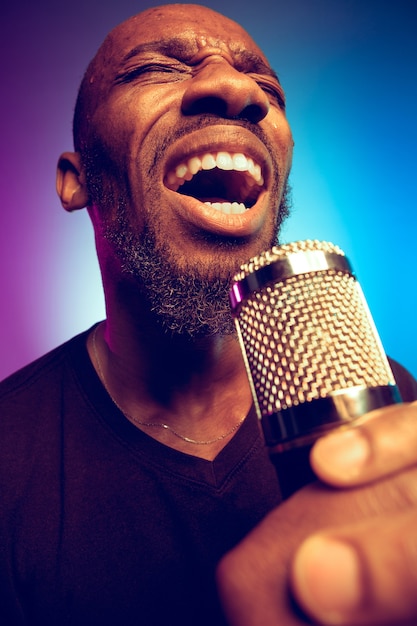 Young african-american jazz musician singing a song on gradient purple-blue