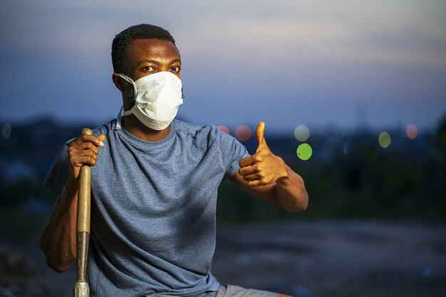 Молодой афроамериканец в защитной маске держит лопату и жестикулирует