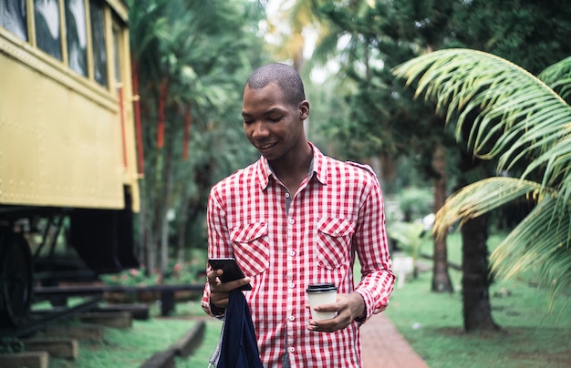 Free photo young african american male in a red and white chequered shirt using his phone in a park