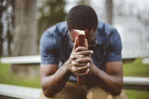 Free photo young african-american male sitting with closed eyes with the bible in his hands