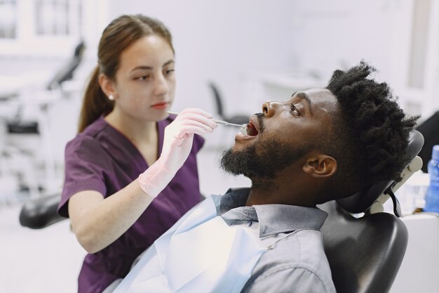 Молодой афро-американский мужчина. Парень посещает кабинет стоматолога для профилактики ротовой полости. Мужчина и семейный врач во время осмотра зубов.