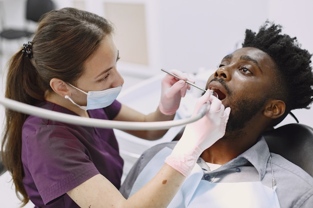 若いアフリカ系アメリカ人の男。口腔予防のために歯科医院を訪れる男。歯の健康診断中の男性と女性の医師。