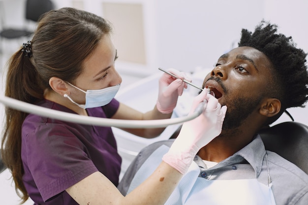 젊은 아프리카 계 미국인 남자. 구강 예방을 위해 치과 의사의 사무실을 방문하는 남자. 검진 치아 동안 남자와 famale 의사.