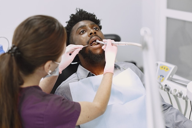 Free photo young african-american man. guy visiting dentist's office for prevention of the oral cavity. man and famale doctor while checkup teeth.