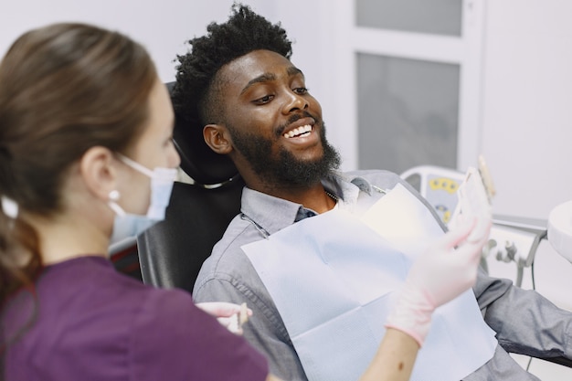 젊은 아프리카 계 미국인 남자. 구강 예방을 위해 치과 의사의 사무실을 방문하는 남자. 검진 치아 동안 남자와 famale 의사.
