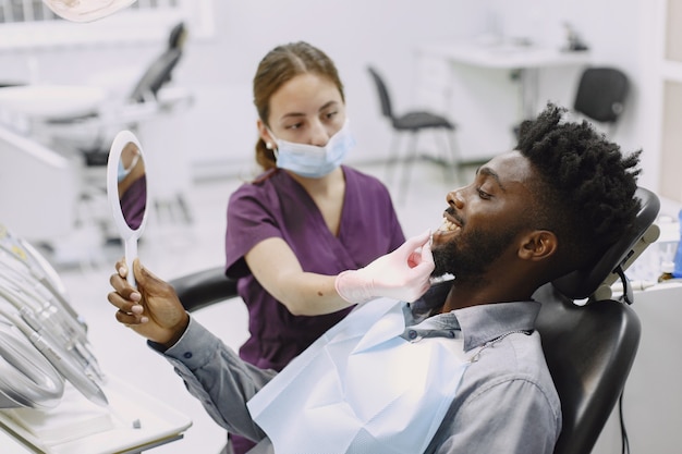 젊은 아프리카 계 미국인 남자. 구강 예방을 위해 치과 의사의 사무실을 방문하는 남자. 검진 치아 동안 남자와 famale 의사.