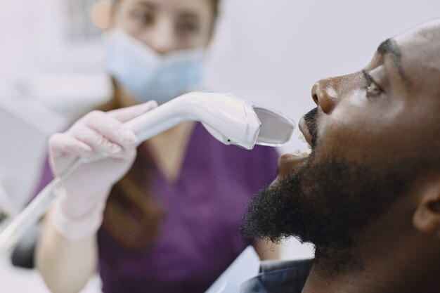 若いアフリカ系アメリカ人の男。口腔予防のために歯科医院を訪れる男。歯の健康診断中の男性と女性の医師。