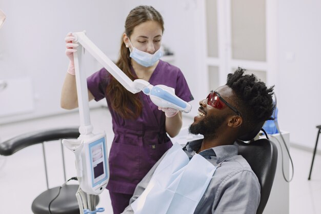 Young african-american man. Guy visiting dentist's office for prevention of the oral cavity. Man and famale doctor while checkup teeth.