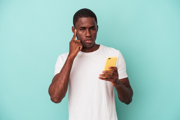 Young african american man holding a mobile phone isolated on blue background pointing temple with finger, thinking, focused on a task.