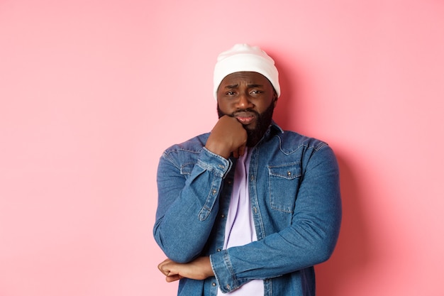 Free photo young african-american man look with pity and concern at camera, frowning and feeling uneasy, standing over pink background