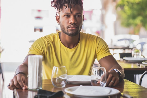 레스토랑에 앉아 있는 동안 카메라를 보고 있는 젊은 아프리카계 미국인 남자.