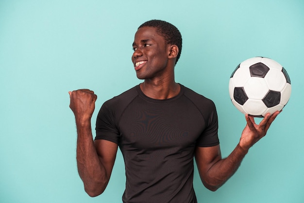 サッカー​を​している​若い​アフリカ系​アメリカ人​の​男​は​、​親指​の​指​を​離れて​、​笑って​のんきな​青い​背景​の​ポイント​で​隔離​。