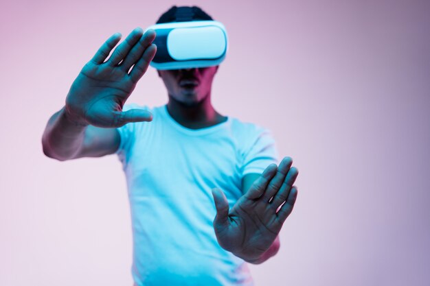 Young african-american man's playing and using VR-glasses in neon light on gradient background