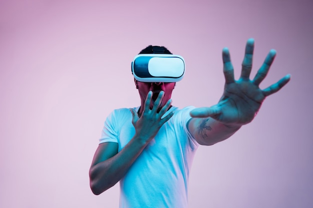 Young african-american man's playing in VR-glasses in neon light on gradient.