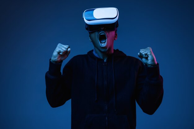 Young african-american man's screaming in VR-glasses in neon on gradient background. Male portrait