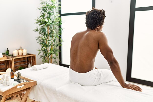 Young african american man sitting on massage board at beauty center