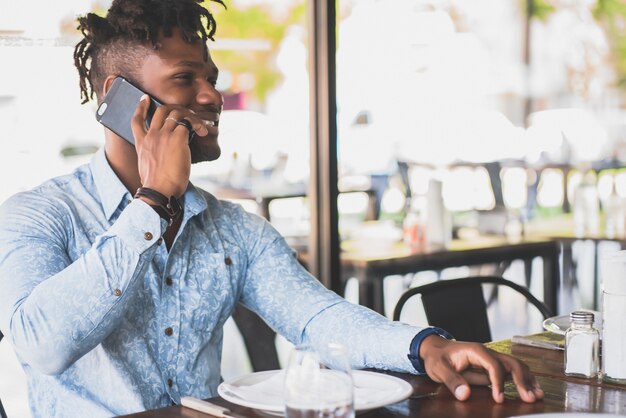 Молодой афро-американский мужчина разговаривает по телефону, сидя в ресторане.