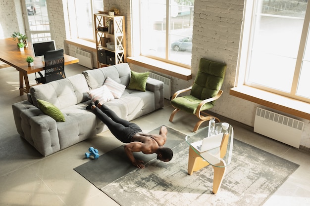 Young african-american man training at home , doing exercises of fitness, aerobic. 