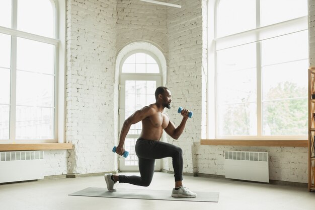 Young african-american man training at home , doing exercises of fitness, aerobic.